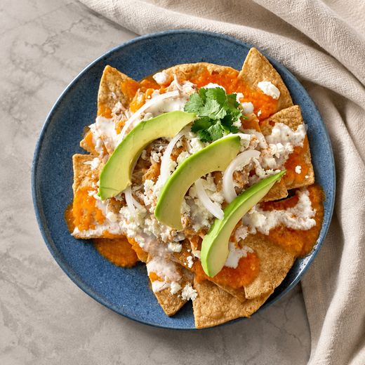 Plato azul con totopos bañados en salsa roja, crema, queso fresco, cebolla y rebanadas de aguacate