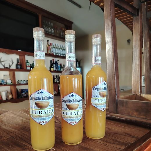 Tres botellas de licor color ámbar sobre la barra de madera, con la estantería de botellas al fondo